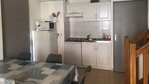 A compact kitchen with white cabinets, a microwave, a sink, and a refrigerator. There is a dining area with a table and chairs. - House in a gated community with heated swimming pool (Mouries)