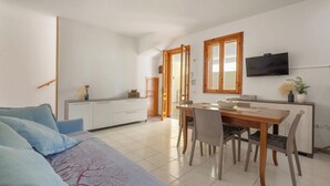 Una sala de estar moderna con un sofá, una mesa de comedor con sillas, una zona de cocina con armarios y un televisor.