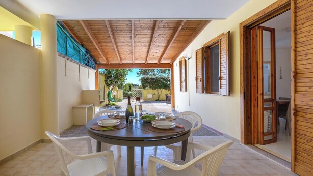 Un patio cubierto con una mesa redonda dispuesta para comer, rodeado de sillas blancas.