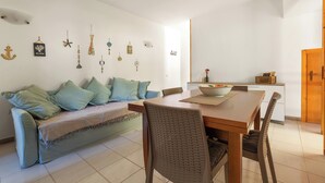 Un comedor con una mesa de madera, sillas, un sofá con cojines y adornos en la pared, incluyendo un cuadro enmarcado y varios objetos colgantes.