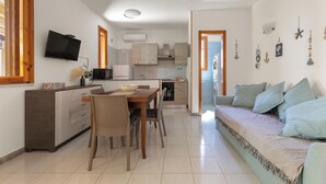 Una cocina moderna con zona de comedor, un televisor montado sobre la encimera y un sofá con cojines.