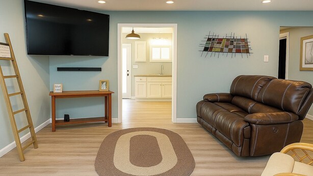 A living room with a brown leather sofa, a wooden coffee table, a TV mounted on the wall, and a patterned rug.