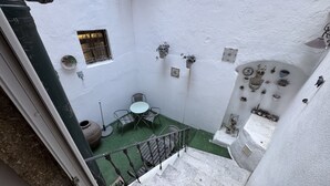Un espacio exterior estrecho con una pequeña mesa y sillas, una planta en maceta y una pared decorada con diversos objetos.