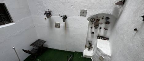 A narrow stairway leading to a room with a green artificial turf floor, white walls, and various potted plants and decorative items.