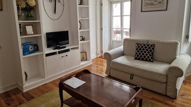 Una sala de estar con sofá, televisor, mesa de centro de madera y un reloj de pared.
