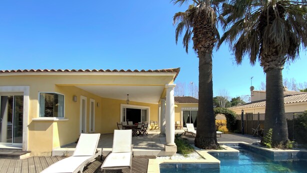 A poolside area with lounge chairs, a covered patio, and a clear blue pool.