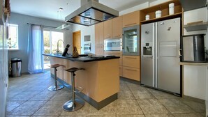 A modern kitchen with a central island, stainless steel appliances, and a view to the outside.