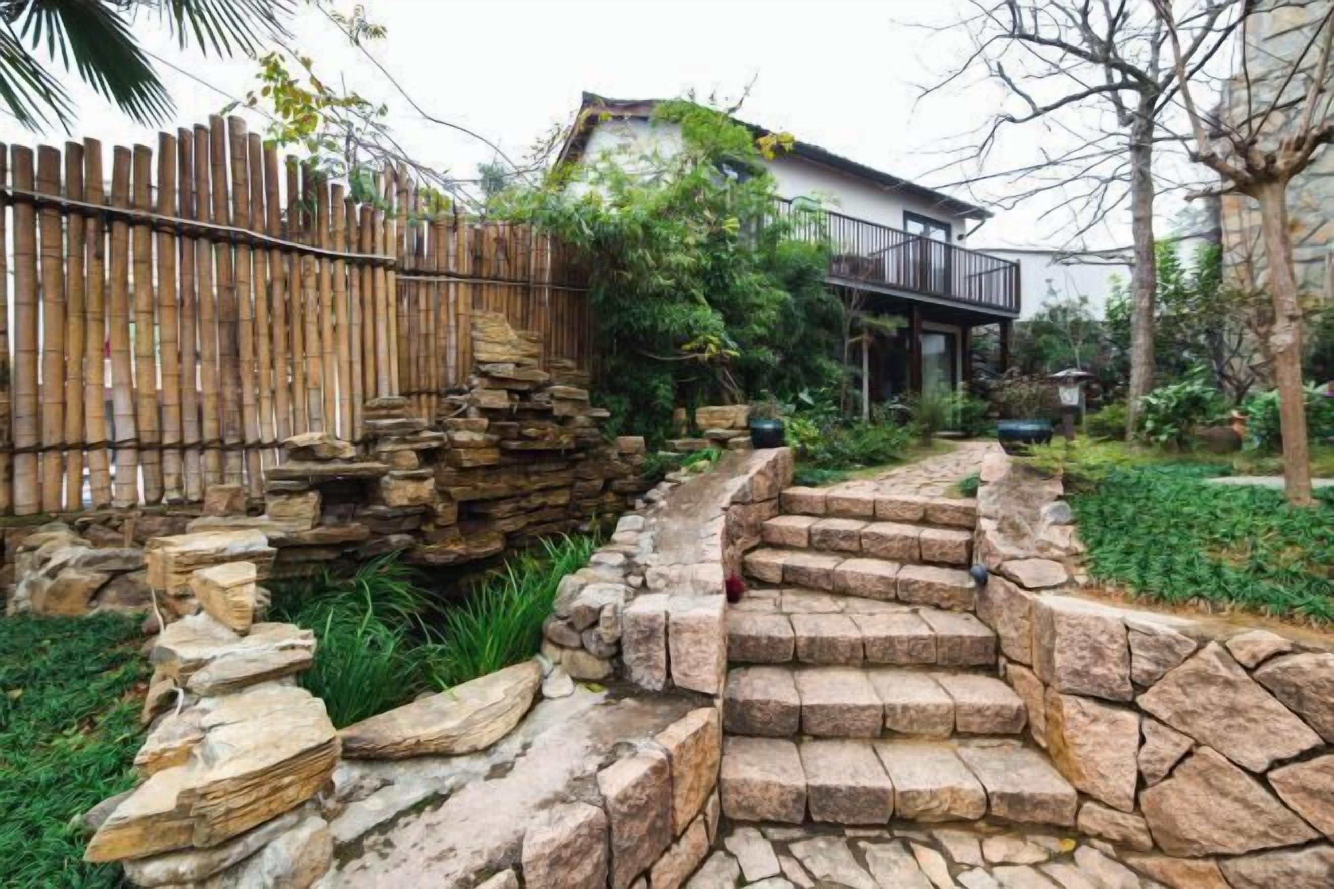 Eine Steintreppe führt zu einem Haus mit Holzzaun und Garten.