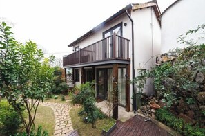 Een modern huis met een balkon, een pad van stenen en een tuin met diverse planten.