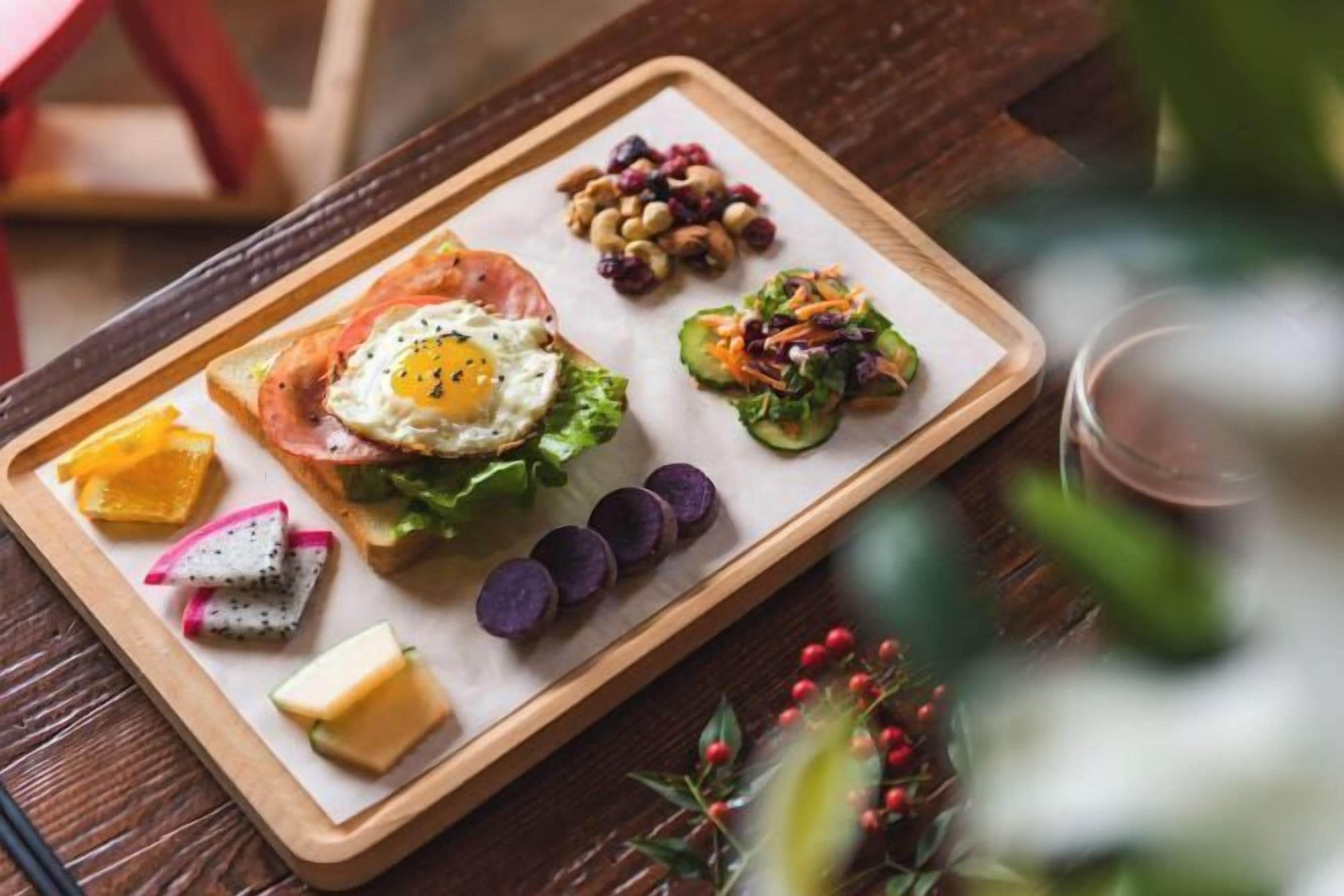 Bandeja de desayuno con tostadas, huevo, aguacate y diversas frutas y frutos secos.