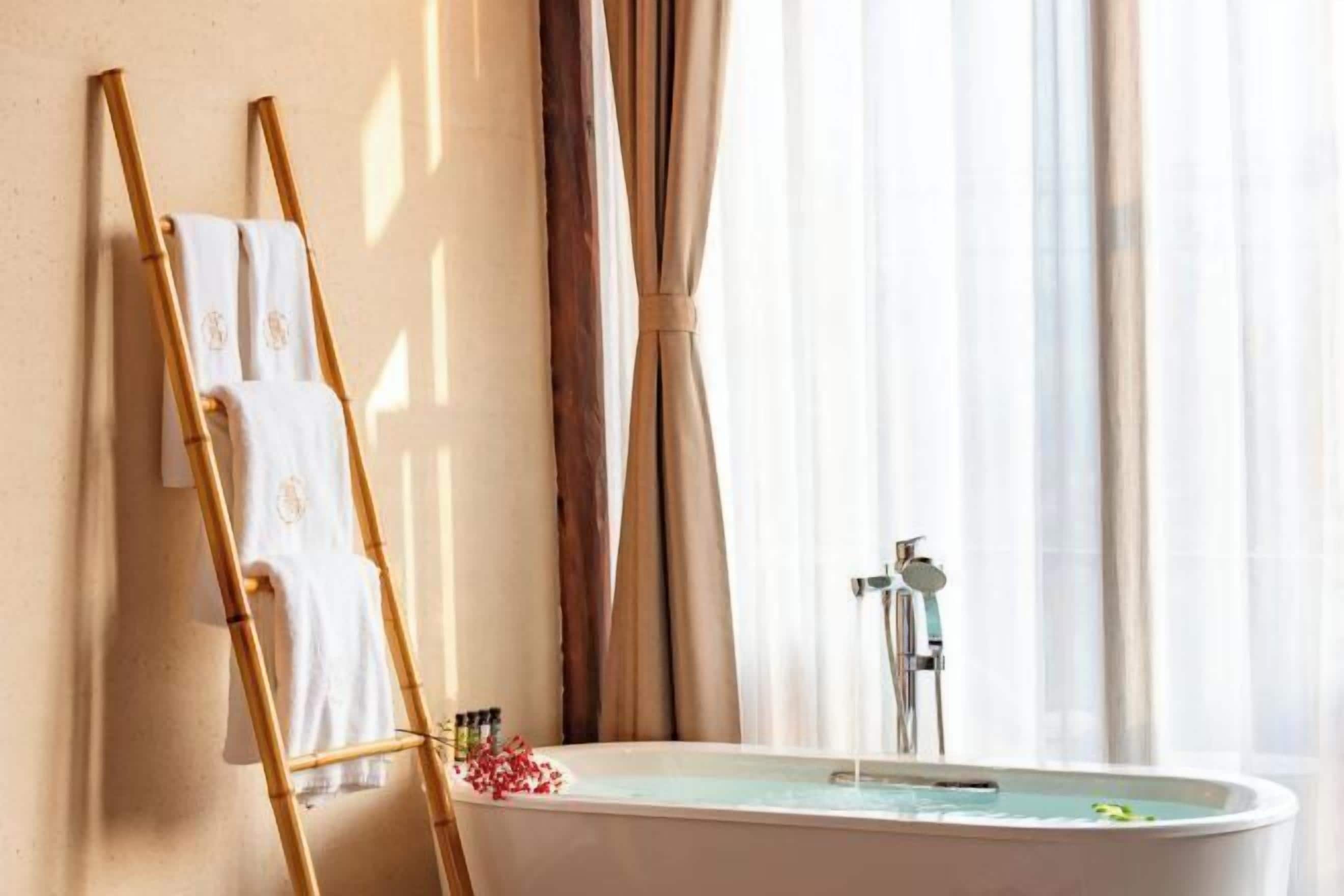 A bathroom with a bathtub, a bamboo ladder, and a set of towels.