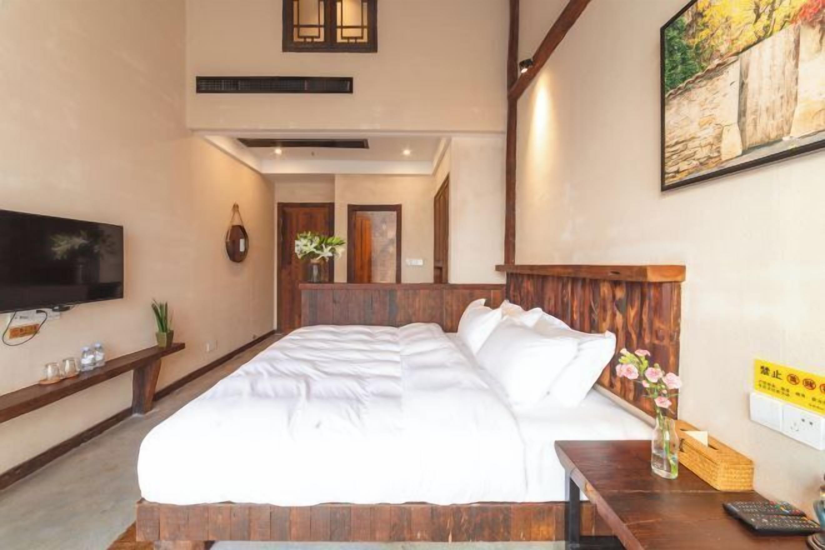 A hotel room with a large bed, wooden headboard, a flat-screen TV, a bedside table, and a painting on the wall.