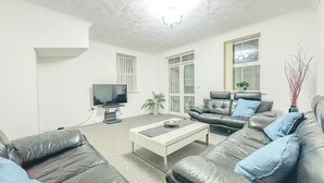 A living room with a flat-screen TV, two leather sofas, a coffee table, and a large window.