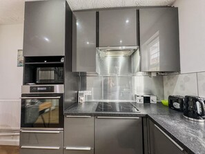 A modern kitchen with stainless steel appliances, a built-in oven, microwave, and a gas stove. - Oakwood House 6 Bed 11 Sleeps Garden-free Parking (Leicester)