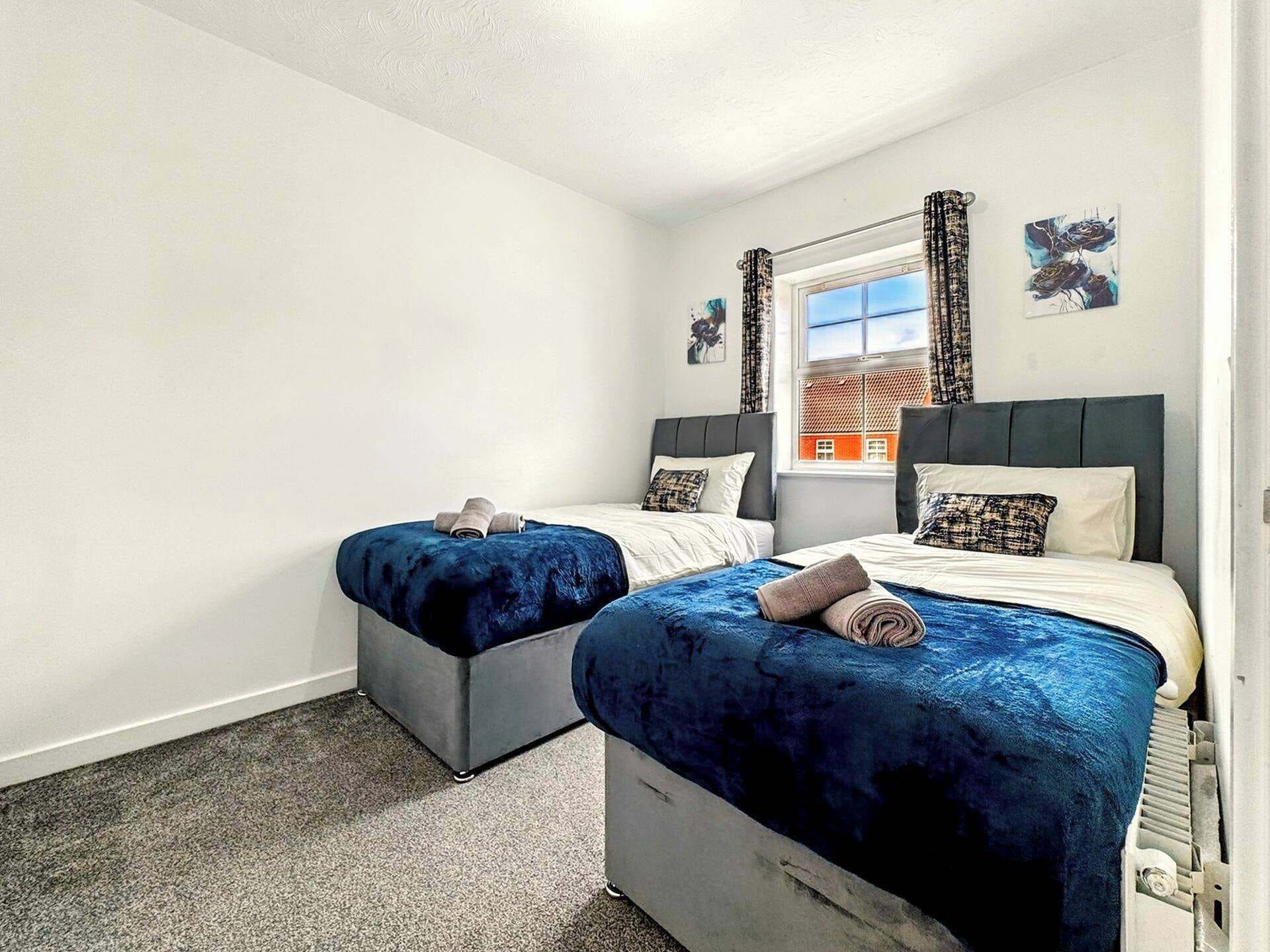 A bedroom with two beds, a window with curtains, and artwork on the wall.