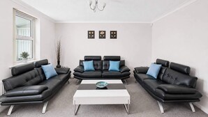 A modern living room with a black leather sofa set, a white coffee table, and a chandelier.