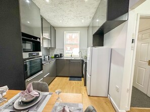 A compact kitchen with modern appliances, a dining area with a table set for two, and a view of the outside through a window. - Oakwood House 6 Bed 11 Sleeps Garden-free Parking (Leicester)