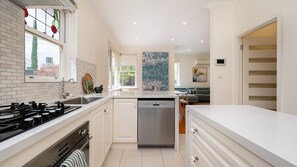 A modern kitchen with white cabinetry, a built-in dishwasher, and a gas stove. - Pet Friendly - Miss Peregrine in Brighton East (Brighton East)