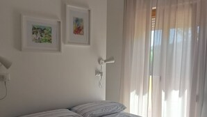 A neatly made bed with striped bedding, a wall-mounted telephone, and two framed artworks.