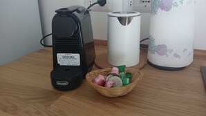 A kitchen counter with a coffee maker, a kettle, and a basket of coffee pods.