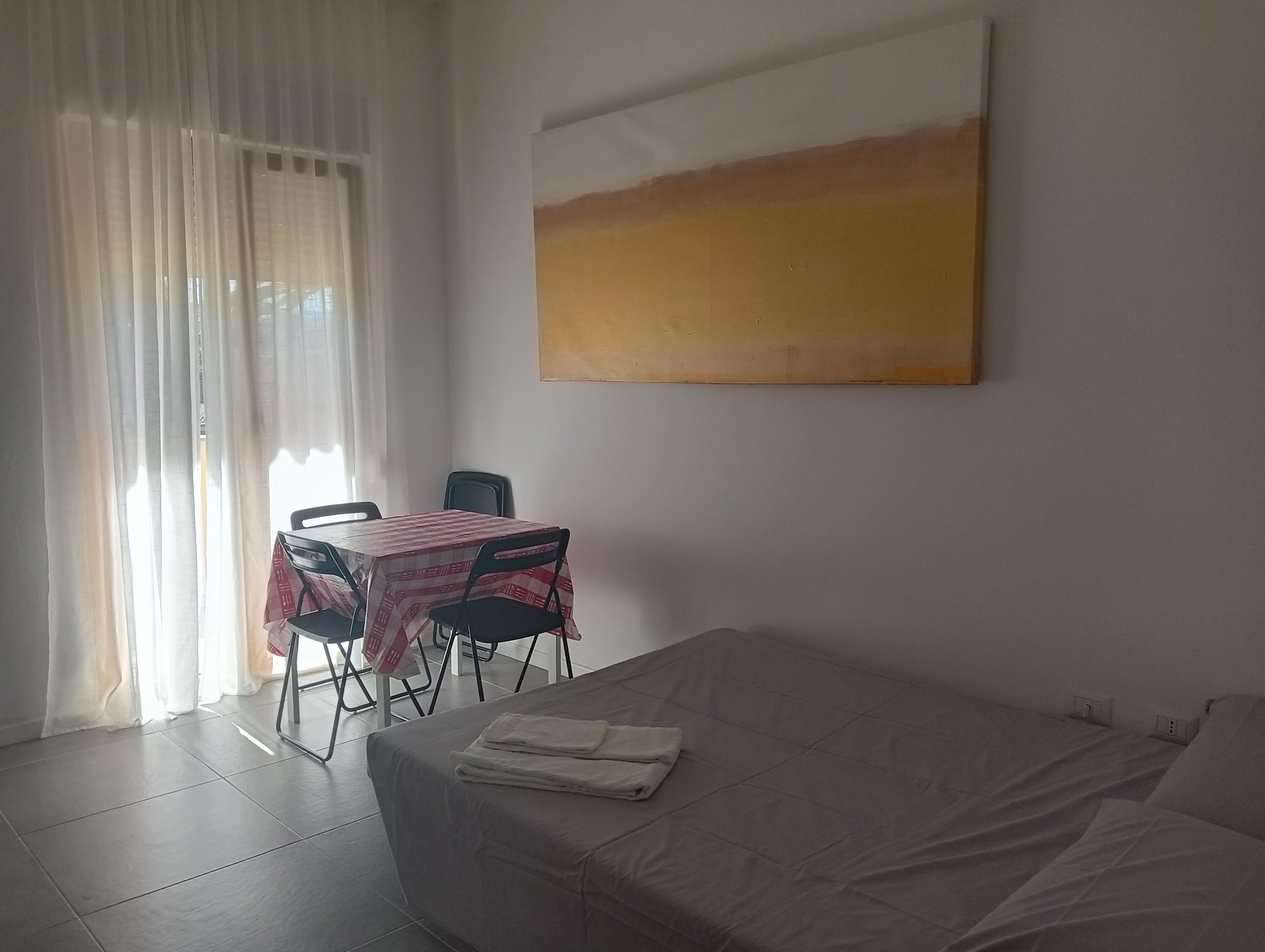 A room with a bed, a table with chairs, a window with curtains, and a painting on the wall.
