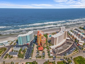A coastal hotel with multiple buildings, a parking lot, and a beach in the background.