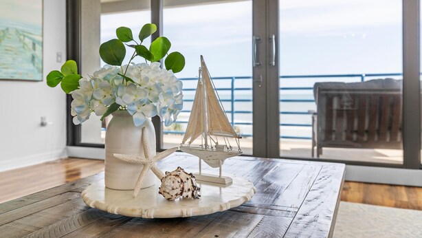 Una mesa con un jarrón decorativo de flores blancas, una estrella de mar, una concha marina y un pequeño barco modelo.