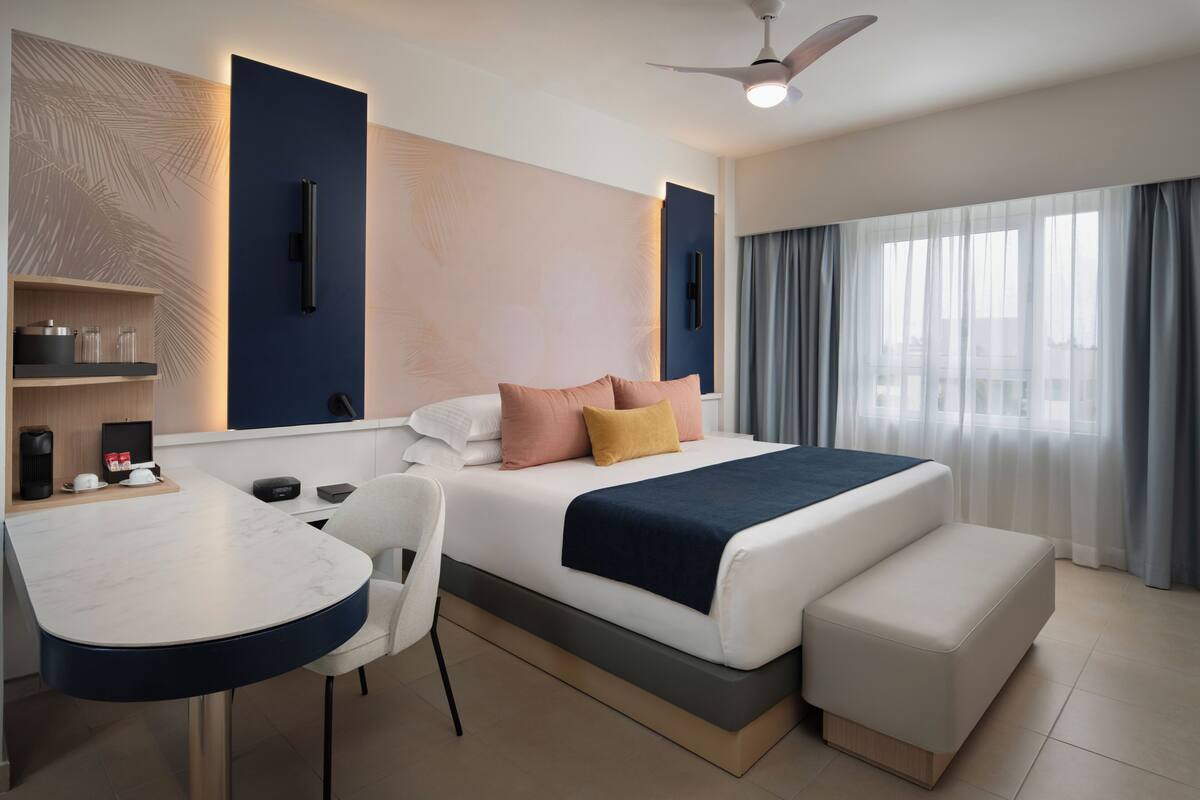 Une chambre d’hôtel moderne, équipée d’un lit, d’une table de chevet, d’une chaise et offrant une vue sur la ville grâce à de grandes fenêtres.