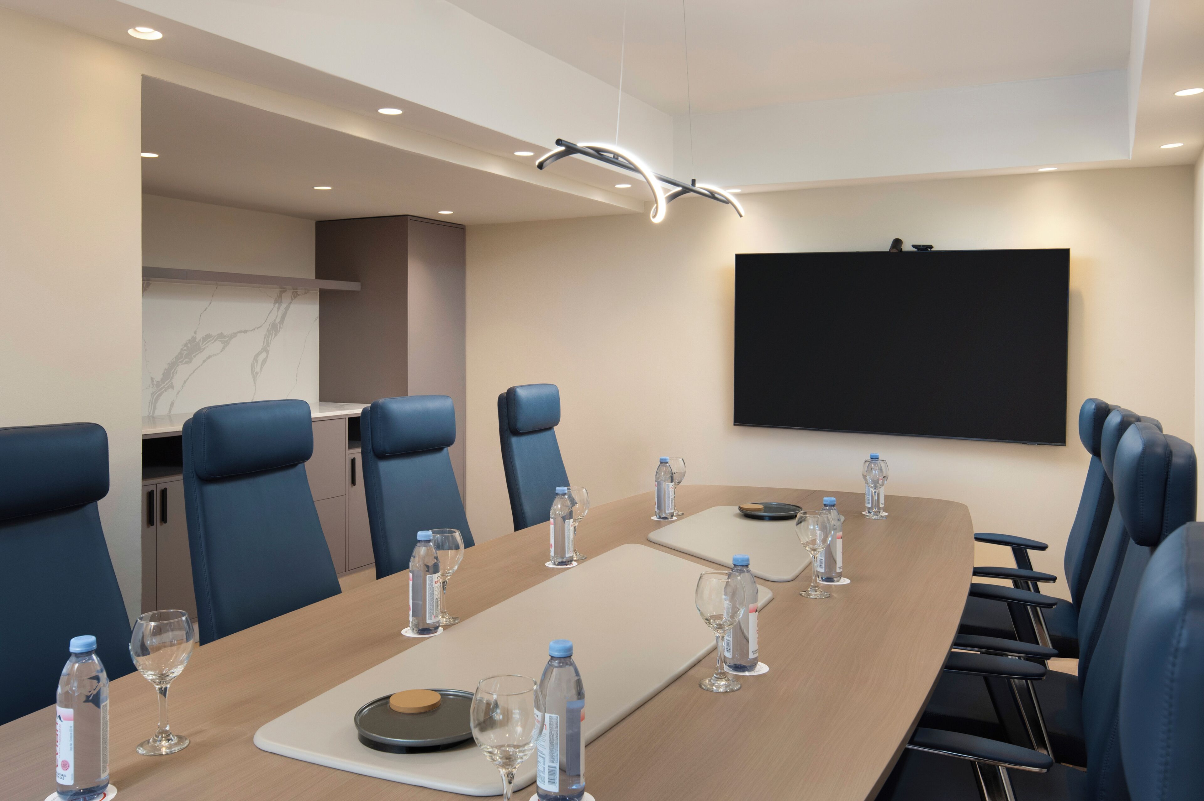 A conference room with a long table, blue chairs, water bottles, and glasses.