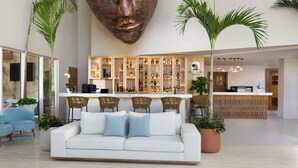 A spacious lobby with a reception desk, a bar area with shelves of bottles, a white sofa with blue cushions, and two large potted plants. - Royal Beach Hotel Punta Cana A Jdv By Hyatt Hotel (Punta Cana)