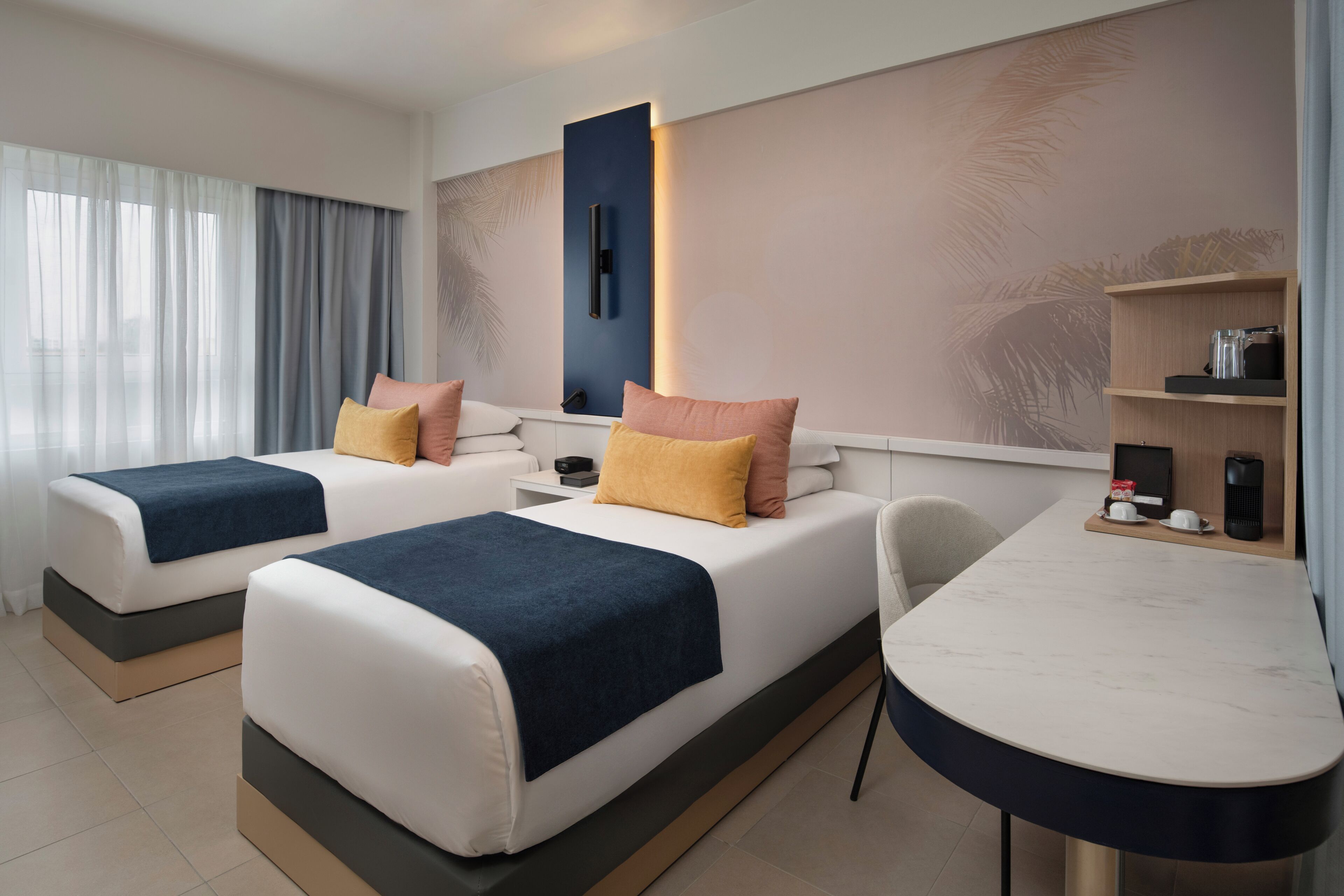 Een hotelkamer met twee bedden, een bureau, een koffieapparaat en een tv aan de muur.