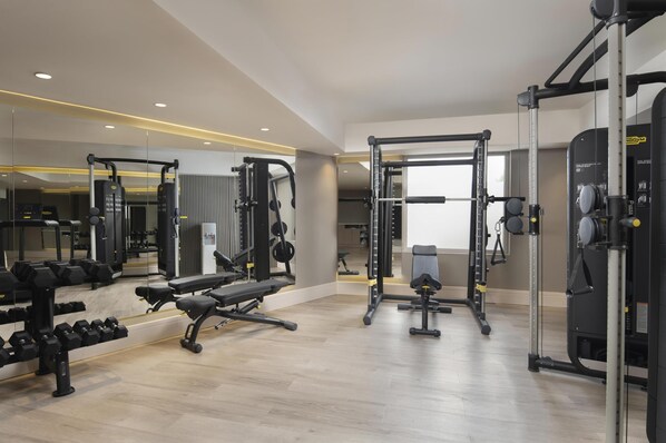 A modern gym with various exercise equipment, a bench, and dumbbells.