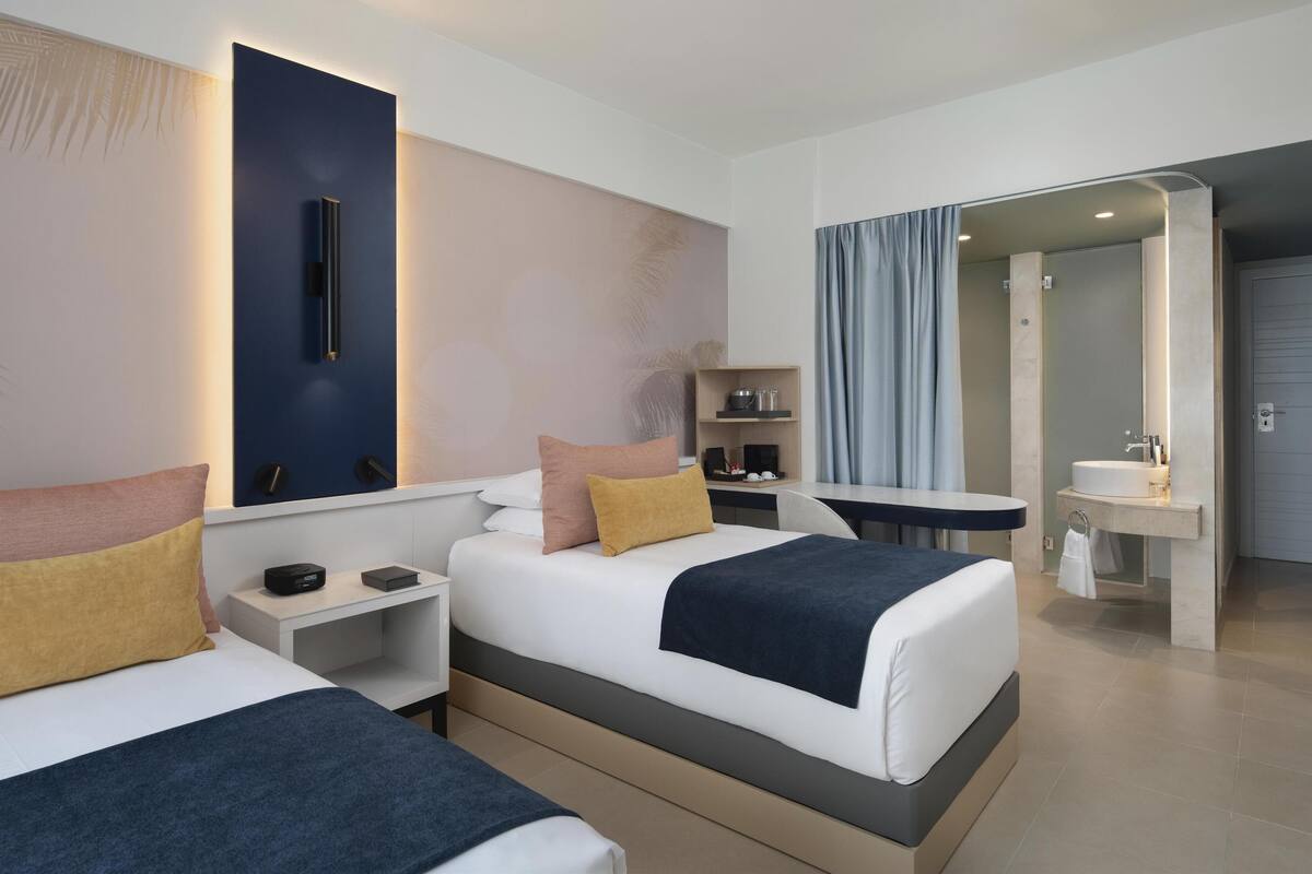 Une chambre d’hôtel moderne équipée de deux lits, d’un bureau, d’une coiffeuse avec miroir et d’un espace douche.
