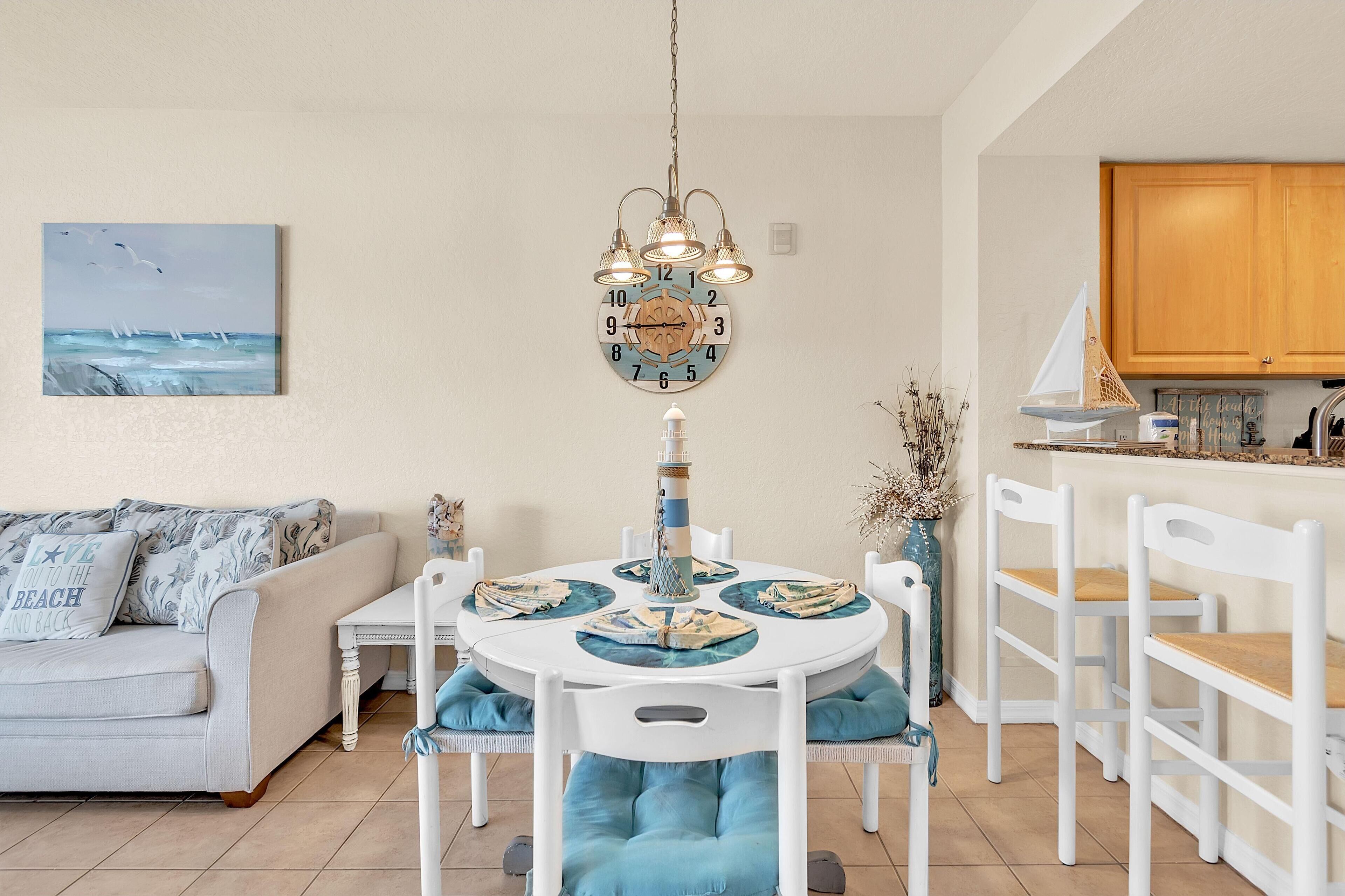 A dining area with a round table, white chairs, and a clock above.