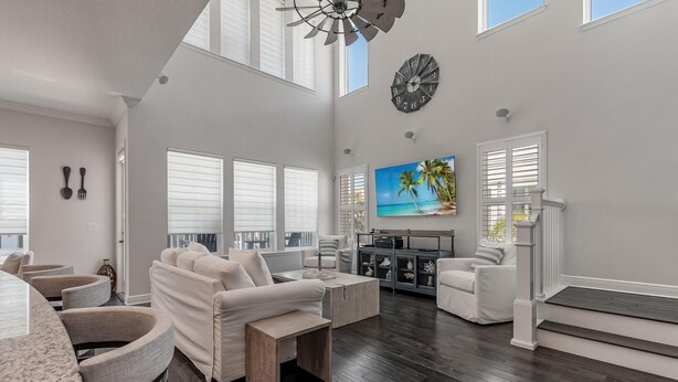 A spacious living room with a large TV, white furniture, and a wooden coffee table.
