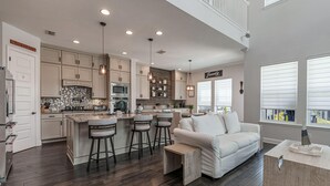 A spacious kitchen with a central island, bar stools, and a white sofa in a modern living area.