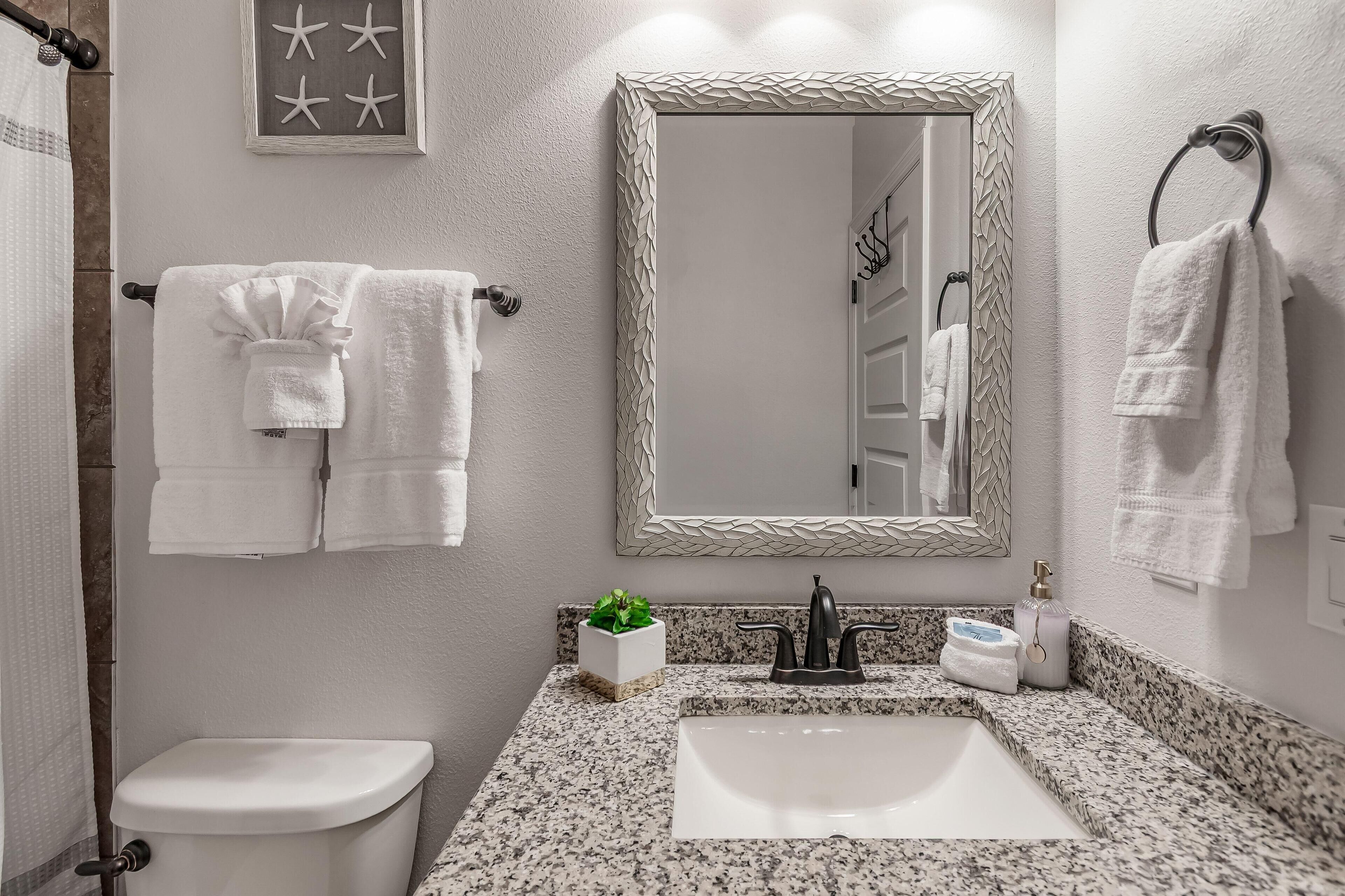 A modern bathroom with a granite countertop, a white sink, a large mirror, and two white towels on towel racks.