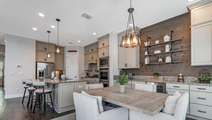 A modern kitchen with a central island, bar stools, and a hanging light fixture.