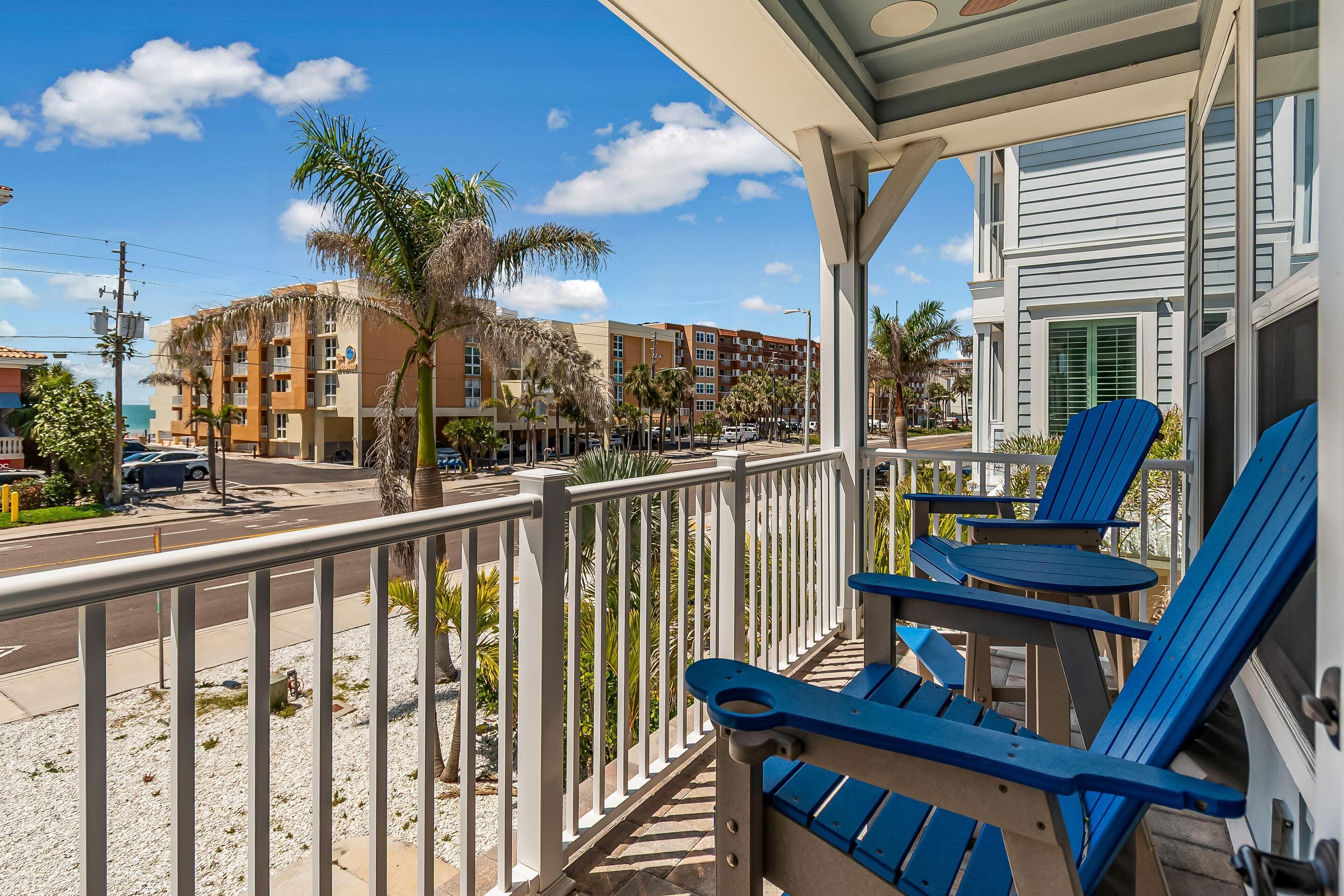 A balcony with blue chairs and a view of a street with palm trees and buildings.