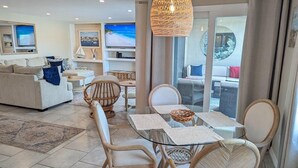 Un salon moderne avec une table à manger en verre, des chaises en osier et un grand téléviseur.
