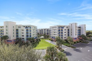 A multi-story hotel with a central courtyard, parking area, and surrounding greenery. - Oceanwalk 1-502 (New Smyrna Beach)