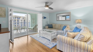 A living room with a glass coffee table, striped sofa, and a ceiling fan.