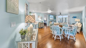 A spacious living area with a glass coffee table, white wicker chairs, and a view of the city through large windows.
