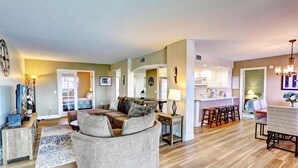 A spacious living room with a large round sofa, a dining area with a table and chairs, and a kitchen in the background. - Bayshore Yacht & Tennis 806 (Indian Shores)