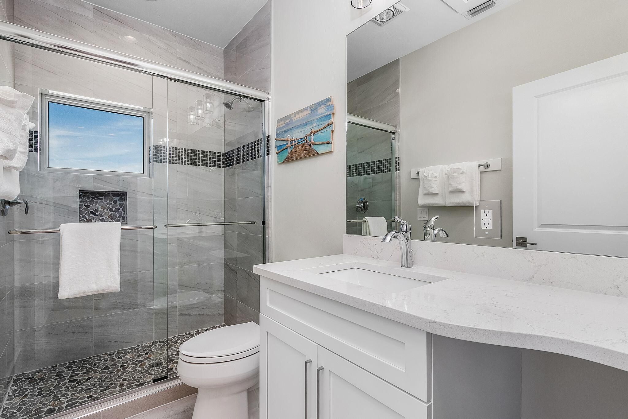 A modern bathroom with a glass shower enclosure, a white toilet, and a marble countertop.