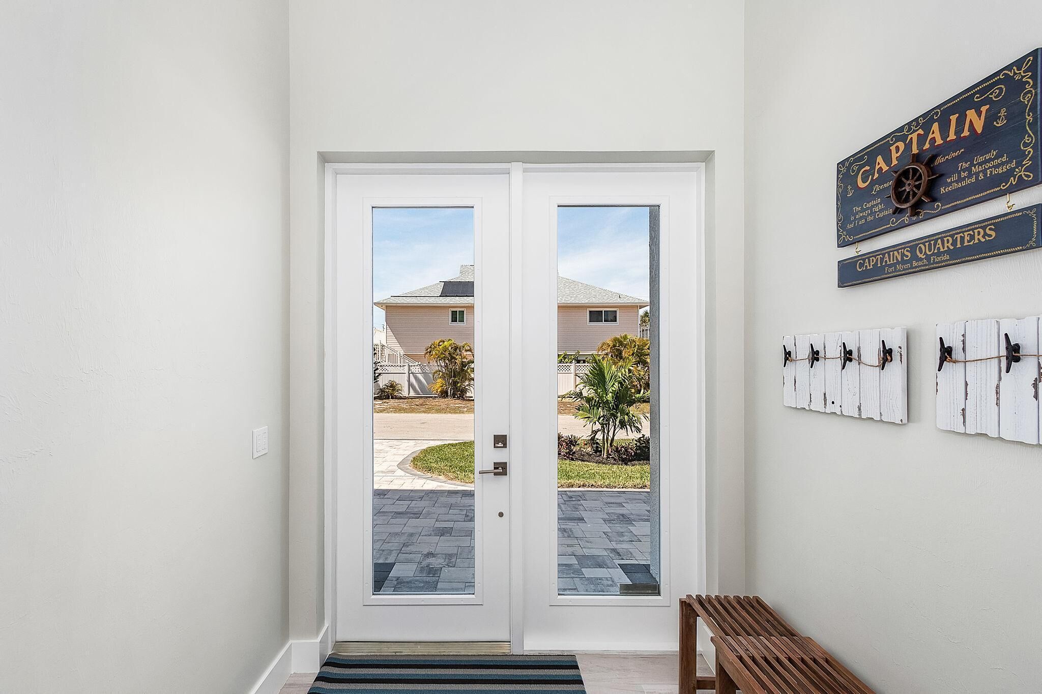 A double door entrance with a view of a residential area, a wooden bench, and a wall-mounted sign reading "CAPTAIN'S QUARTERS".