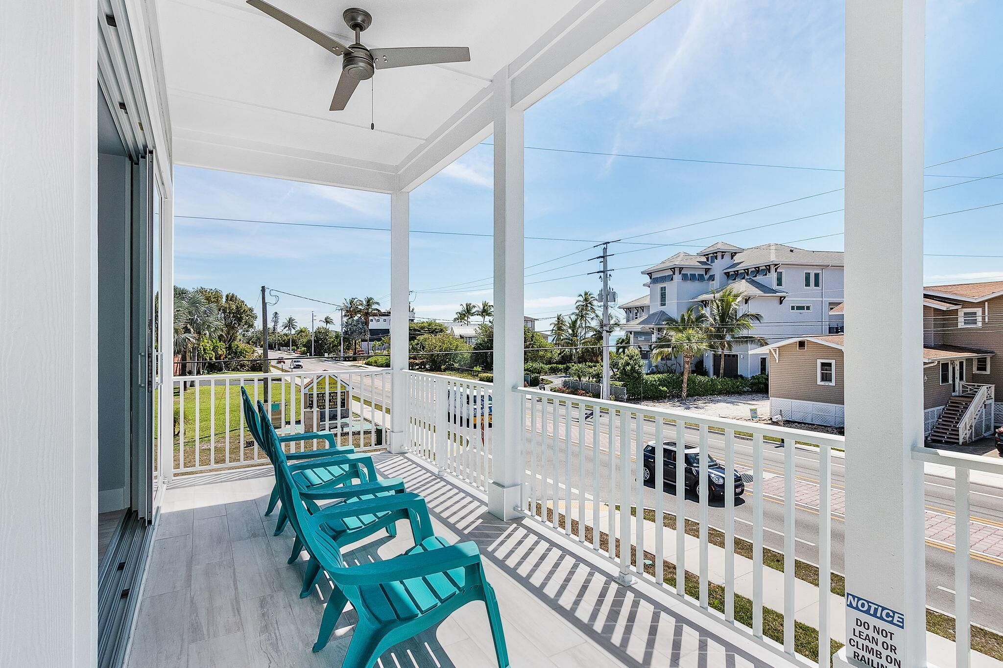 A covered balcony with teal chairs, a ceiling fan, and a view of a residential street.