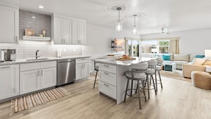 A modern kitchen with white cabinets, a central island with stools, and a dining area with a sofa and coffee table. - Seaward B503 (New Smyrna Beach)