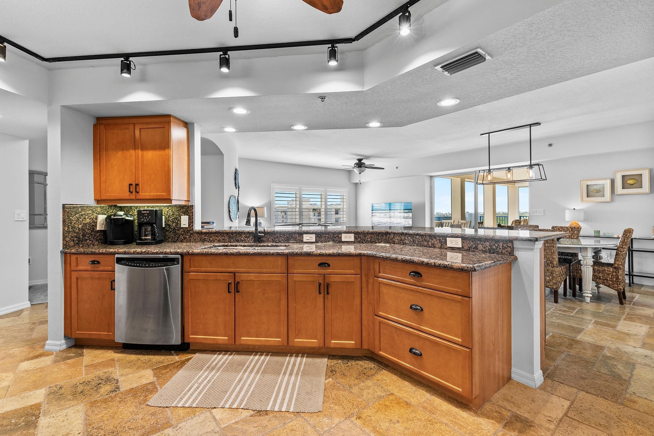 A modern kitchen with wooden cabinets, a stainless steel dishwasher, granite countertops, and a large island.