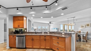 A modern kitchen with wooden cabinets, a stainless steel dishwasher, granite countertops, and a large island. - Oceanwalk 10-601 (New Smyrna Beach)